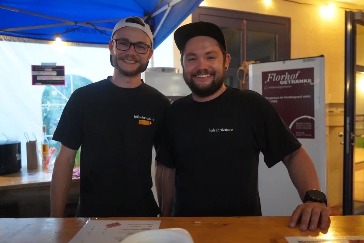 Zwei Männer stehen hinter dem Tresen und lächeln in die  Kamera.